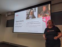 Donna Benjamin stands in front of a screen displaying a screenshot of an article by Shannon Mitchell, published 18 May 2020 called "The forgotten feminist history of agile development" and a quoted snippet saying "Open doors, rather than selling keys" with portraits of Sister Corita Kent, and Octavia Butler. Photo by Fiona Tweedie